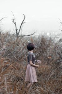 Side view of woman standing on grassy field against sky