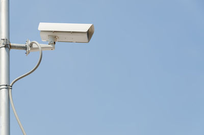 Low angle view of security camera on pole against clear blue sky