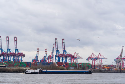 Cranes at harbor against sky