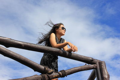 Low angle view of young woman looking away against sky
