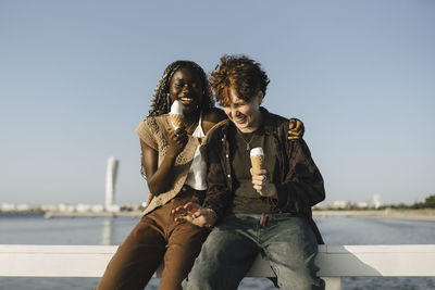 Teenage boy and young woman holding ice cream while sitting on railing