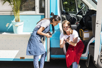 Happy young multi-ethnic female owners sharing smart phone against food truck