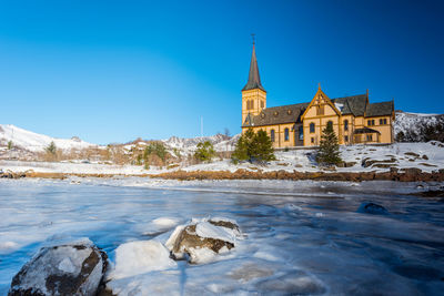 View of building by river against blue sky during winter