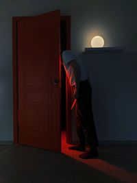 Man with knife looking through door in illuminated room at home