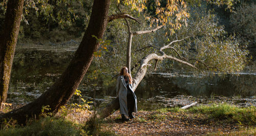 Side view of woman standing by tree trunk in forest