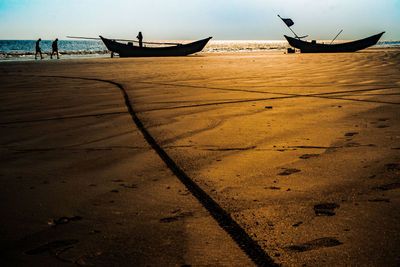 Boat moored on beach against sky during sunset