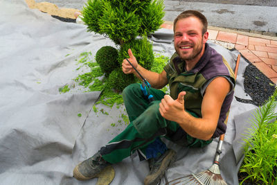 Portrait of smiling mid adult man showing thumbs up while sitting in garden 
