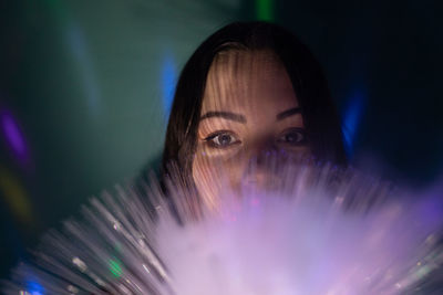 Close-up portrait of young woman holding illuminated fiber optic in darkroom