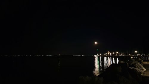 Illuminated city by sea against clear sky at night