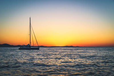 Silhouette sailboat sailing on sea against clear sky during sunset