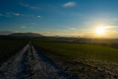 Road amidst field against sky during sunset