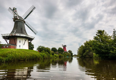 Traditional windmill by lake against sky