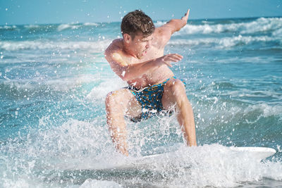 Rear view of shirtless boy splashing water at beach