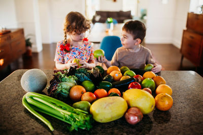 Young boy and girl sitting in kitchen with counter full of fruit