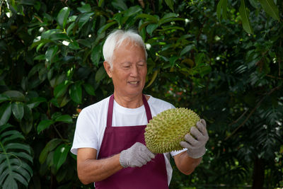 Man holding durian while standing against plants