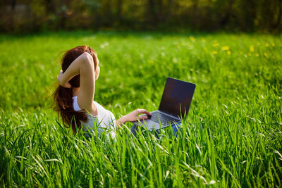 Woman using laptop while sitting on grassy field