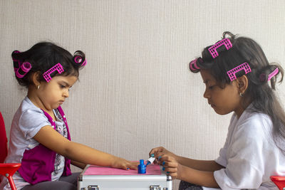 Girl applying nail polish to sister on briefcase at home