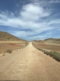 Dirt road along countryside landscape against sky