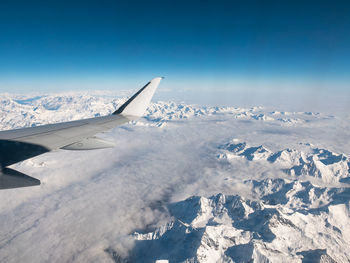 Aircraft wing over snow covered landscape against blue sky