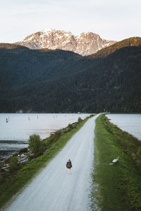 Woman walking on road amidst lake against mountains