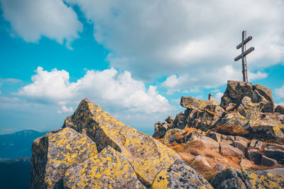 Low angle view of cross on rock against sky