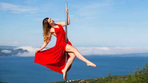 Young woman with red umbrella against sky