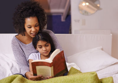 Mother reading story book for daughter on bed