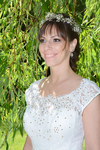 Smiling young woman wearing wedding dress standing against plants