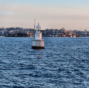 Lighthouse by sea against buildings in city