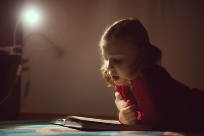 Girl reading book while lying on carpet at home