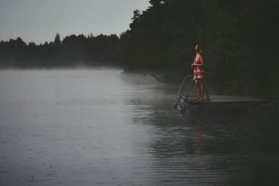 Woman standing on pier in lake against sky