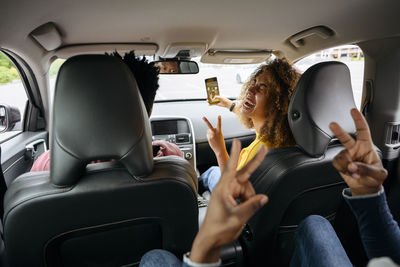 Cheerful woman taking selfie with friends on smart phone in car