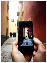 Cropped image of person photographing alley amidst buildings