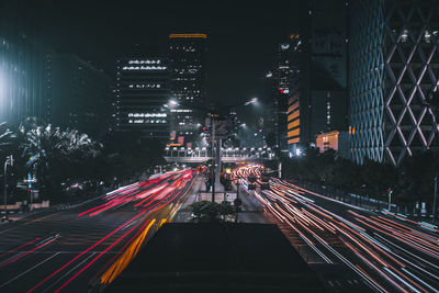 Light trails on road amidst illuminated buildings in city at night