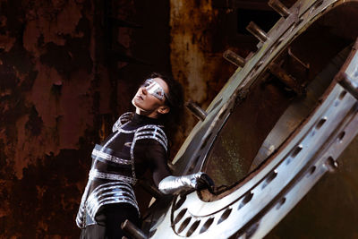 Strong woman in silver glasses and futuristic dress stands against the smoke in destroyed factory