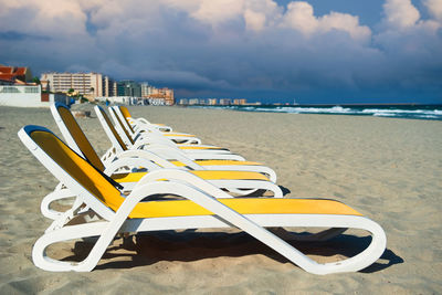 Lounge chairs at beach against cloudy sky