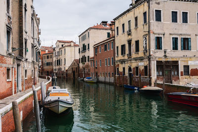 Boats moored in canal amidst buildings in city