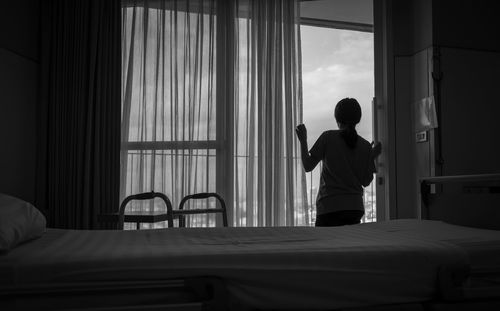 Rear view of woman looking through window at hospital