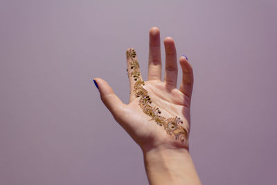 Cropped hand of woman with henna tattoo against purple background