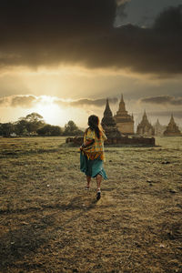 Rear view of woman on field against cloudy sky