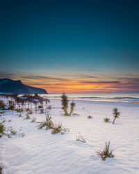 Scenic snow view of sea against sky during sunset