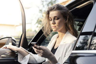 Young woman looking through smart phone while sitting in car