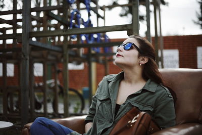 Young woman wearing sunglasses sitting on chair at backyard