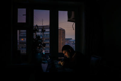 Side view of a man sitting by the window at night
