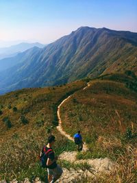 Hikers walking on trail leading towards mountains against clear sky