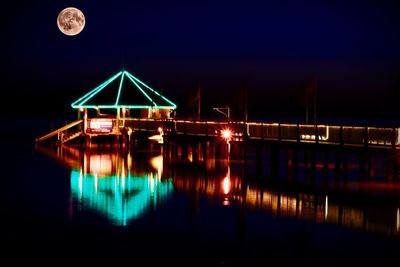 Reflection of illuminated lights in lake against sky at night