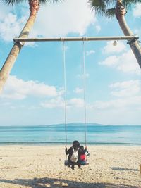Children on swing at beach against sky
