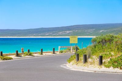 Road by sea against clear blue sky