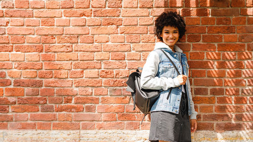 Portrait of smiling teenage girl standing against brick wall
