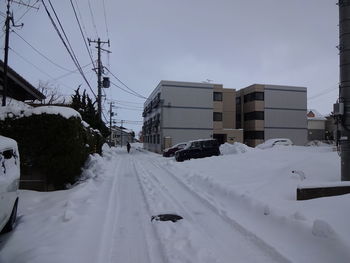 Snow covered road amidst buildings in city